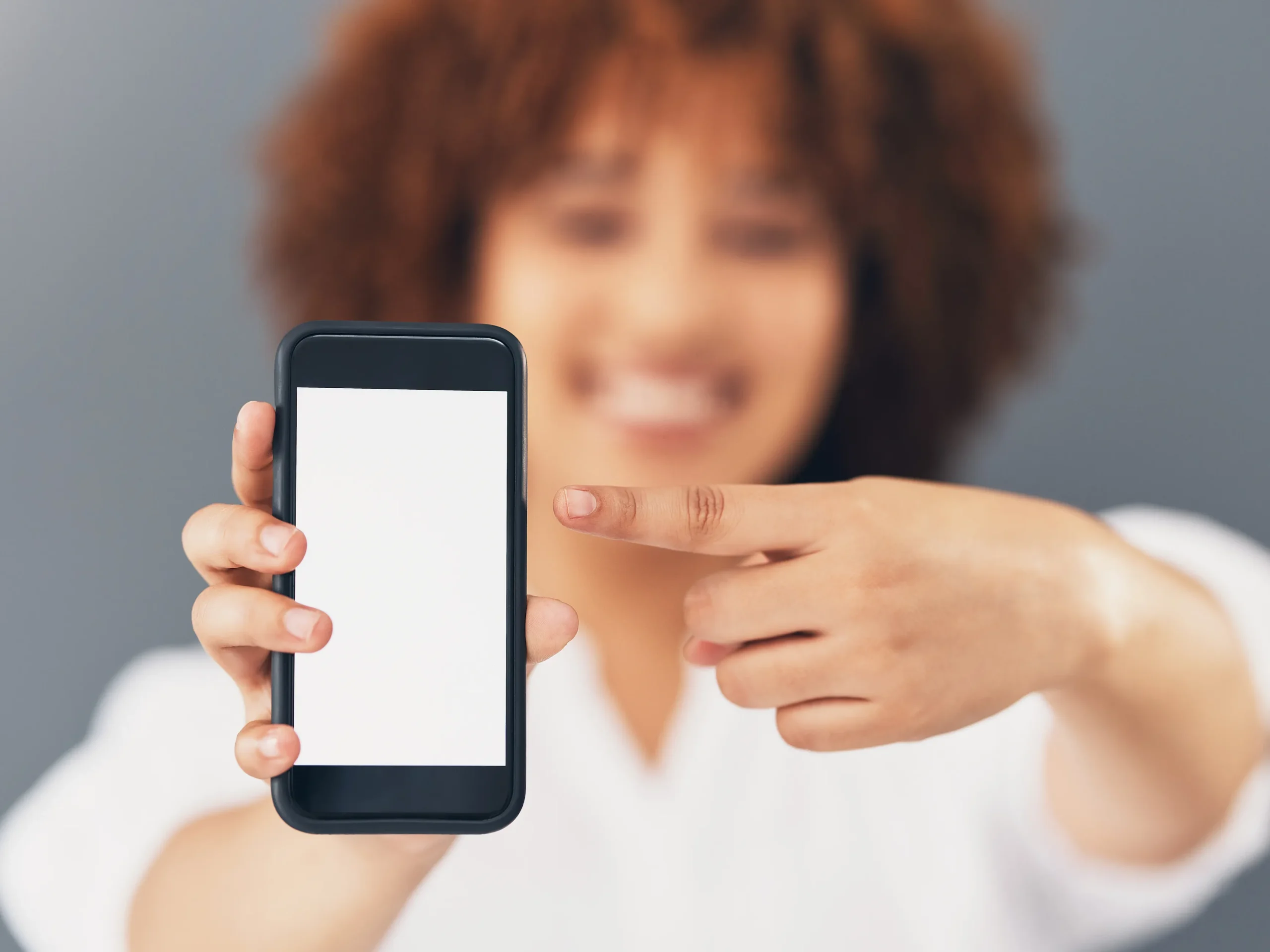 Mujer sosteniendo su teléfono móvil mientras señala la pantalla, simbolizando el control de cuenta en una agencia fanvue