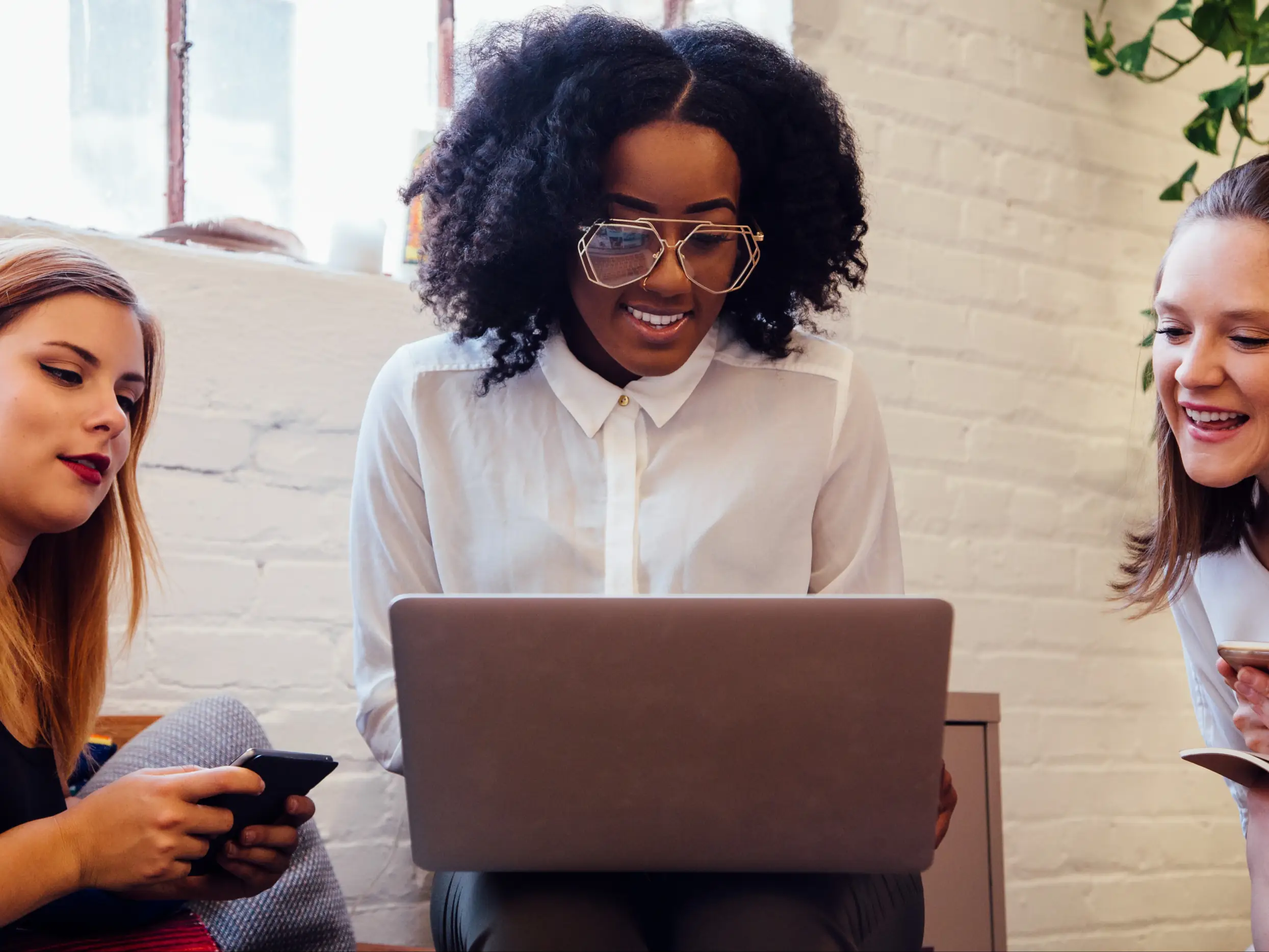 Tres mujeres sonriendo juntas frente a una laptop, representando el acompañamiento cercano de nuestra agencia fanvue a sus modelos