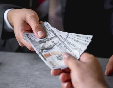 Manos intercambiando billetes representando las ganancias de una creadora en Fanvue