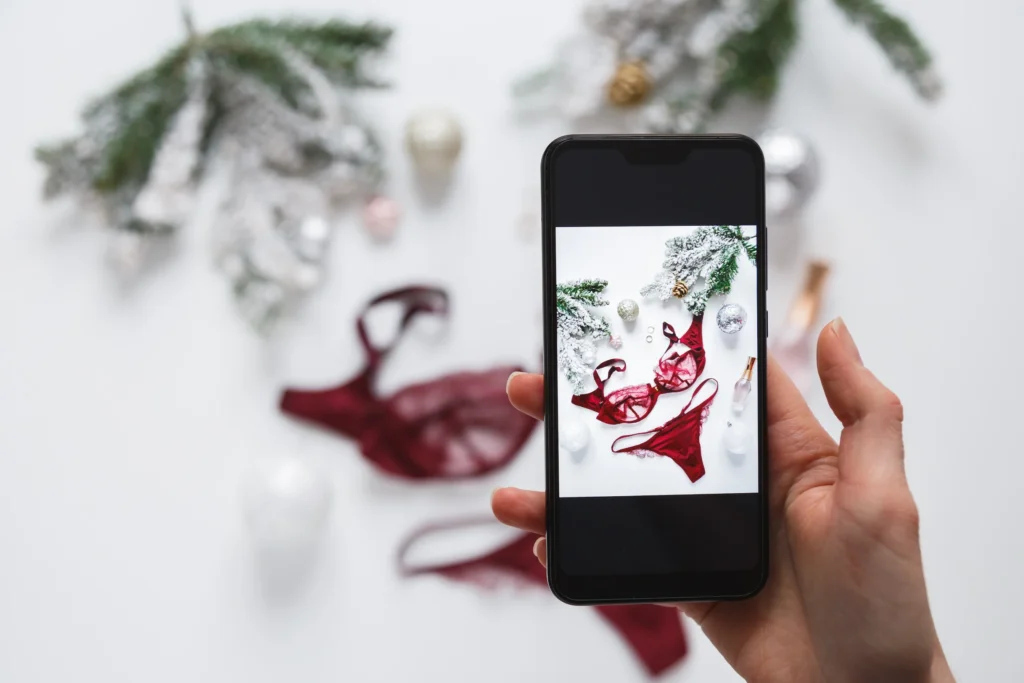 Mano de mujer sosteniendo un móvil fotografiando lencería roja, representando a una creadora de contenido preparando material para Fanvue