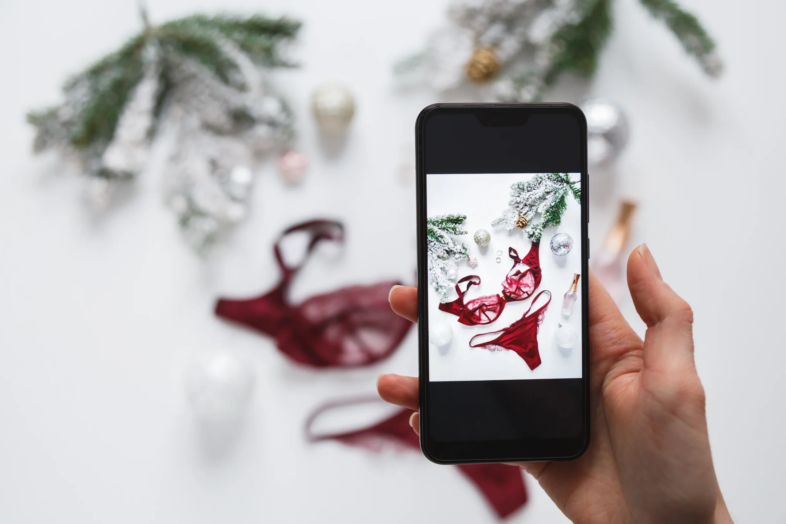 Mano de mujer sosteniendo un móvil fotografiando lencería roja, representando a una creadora de contenido preparando material para Fanvue